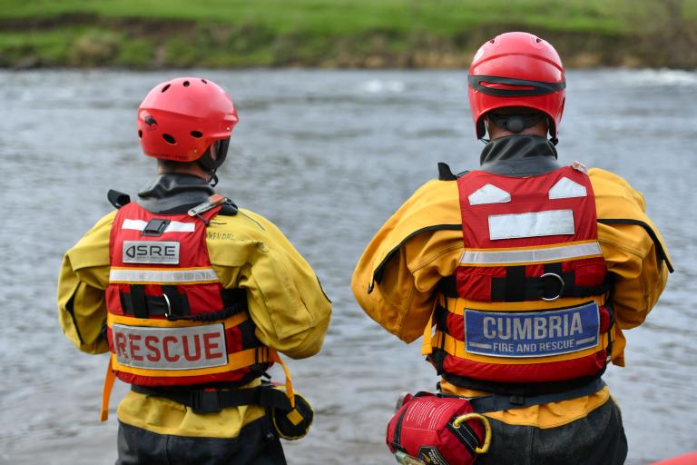 Two firefighters in Swiftwater Rescue Technician (SRT) PPE stood by the water's edge.